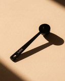 Black, metal measuring spoon with 'GAYA' branding on a beige background