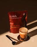 GAYA Functional Mushroom Blend pouch beside a glass of frothy cacao drink on a dark background