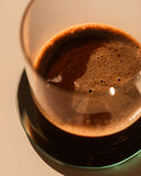 Close-up of a creamy, foam-topped cacao drink in a glass on a beige background